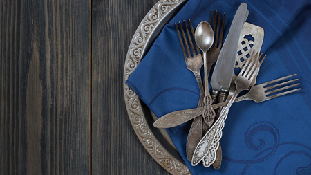 Vintage metal flatware on the old metal tray with pattern on the edge with blue tray cloth on the black wooden texrured background. Top view  horizontal 9 x 16 shot. Grey and blue colour. tray is on the right part of the shot. Left is for Copy space.の写真素材