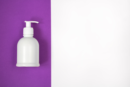 White plastic dispenser bottle with shadow and without label lays down on the bright ultra violet vertical left half of rightangle horizontal background, the other part is white for copy space. Top view.の写真素材