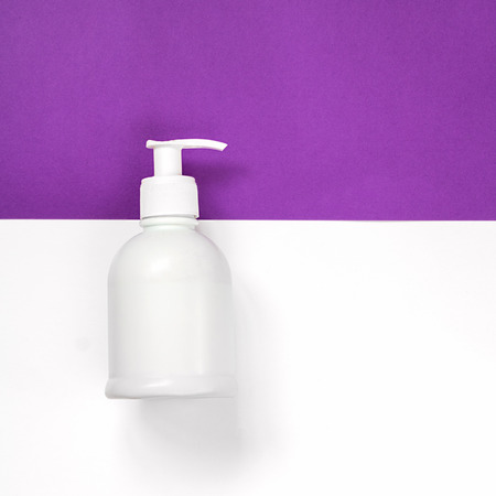 White plastic dispenser bottle with shadow and without label lays down vertically, upper part on the bright ultra violet horizontal half of square background, the other is on white. copy space. Top view.の写真素材