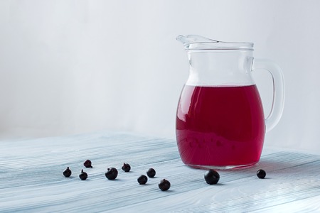 small glass decanter with bright red black currant beverage stands on white and blue wooden textured background and some currants on it white background behind. camera angle 0 degrees. Copy space.の写真素材