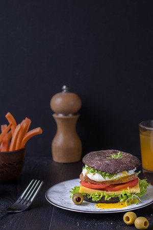 Burger with tomato, egg and Fresh Greens on a plate on a dark background with copy spaceの写真素材