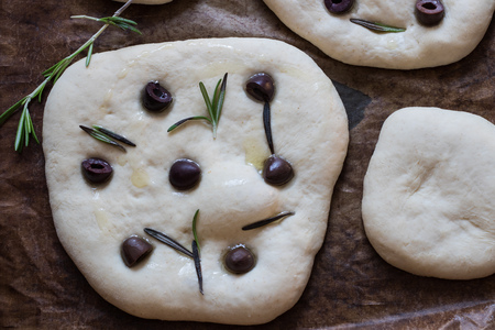 Traditional raw Italian Focaccia with black olives and rosemary - homemade flat bread focacciaの写真素材