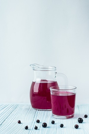 small glass decanter and glass with bright red currant beverage stands on white and blue wooden textured background and some currants on it white background behind. camera angle 0 degrees. Copy space. Vercicalの写真素材
