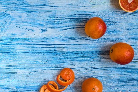 Red oranges, one is cut and mandarines and spiral skin on the textured wooden white and bright blue with cracks bachground. Diagonal. horizontal. Top view. Copy space.の写真素材