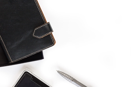 Leather closed two notebooks with clips with orange stitch on edges half seen put diagonally, mobile phone and grey pen on the left side of horizontal shot on the empty white background for copy space top viewの写真素材