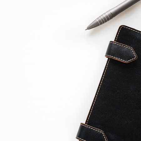 Leather closed notebook with clips with orange stitch on edges half seen put diagonally and grey pen on the right side on of square shot on the empty white background for copy space top viewの写真素材