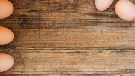 Five eggs on wooden brown old textured background. Five eggs, three in line on the left edge and two in the upper corner. Easter background with copy space for text. Horizontal banner.の写真素材