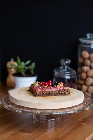 A piece of festive nut pie with cream and candied berries and shelled walnuts on the defocused glasscans with walnuts, cinnamon mill and green plant on the backgroundの写真素材