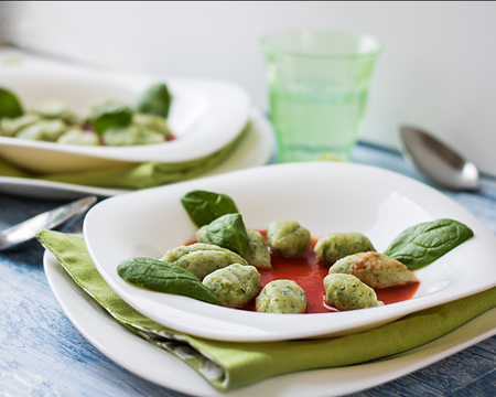 Green ricotta and spinach gnocchi with tomato sauce on the served tableの写真素材