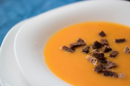 Bright orange pumpkin cream soup with rye croutons on blue stone backgroundの写真素材