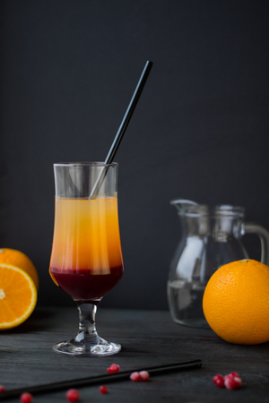 layer orange and red coctail with straw and defocused oranges on the black backgroundの写真素材