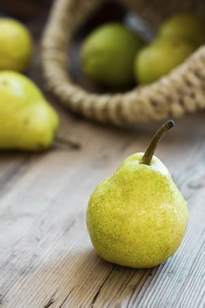 one fresh ripe organic yellow pear on rustic wooden brown table with defocused pears in basket on background. Selective focus. Vertical copy space. For design about agricilture, fruit and healthy foodの写真素材