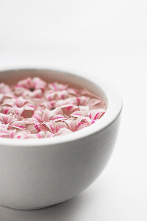 White bowl with water with pink hyacinth flowers and falling drop of water on white blank background. Verticalの写真素材
