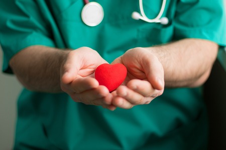 male doctor in green costume with stethoscope holds in hands bright red heart in the center of the shot. Horizontal, healthcare, medicine, preventive treatment,の写真素材