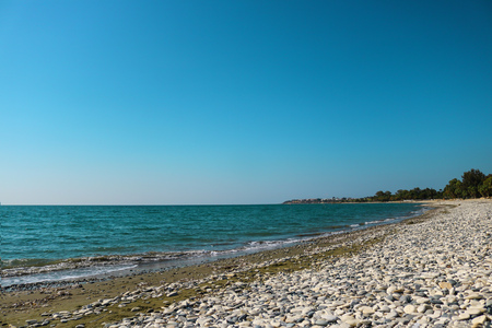 empty sea shore with white pebble, Landscape sand and round sones on the shore, trees far away, sea and blue sky. Travel. Unpopular place not for tourists. Cyprus, Mediterranian, Larnaca, Pervolia, Meneuの写真素材