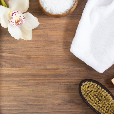 woman massage, body and skincare and bath products, sea salt in bowl, white towel, flower, cacus brush for dry massage on brown wooden background. Beauty blogger cosmetics Copy space Mockup Squareの写真素材