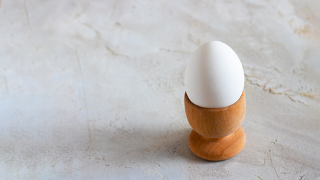 White Breakfast egg in wooden egg cup on grey cement textured background, Horizontal banner, Copy spaceの写真素材