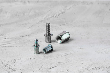 Two metal pop Rivet fasteners of different size, on grey cement background. Horizontal with copy...