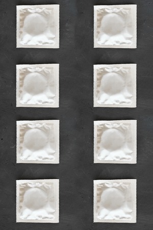Many foil grey square mock up condom packs on black chalkboard background, seamless texture, pattern for health protection from HIV, sexually transmitted diseases, unwanted pregnancy. Top viewの写真素材
