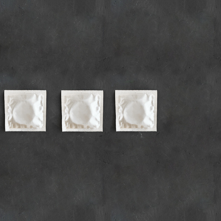 Line of three foil grey square mock up condom pack on empty black chalkboard background with copy space health protection from HIV, sexually transmitted diseases, unwanted pregnancy. Safe sex Top viewの写真素材