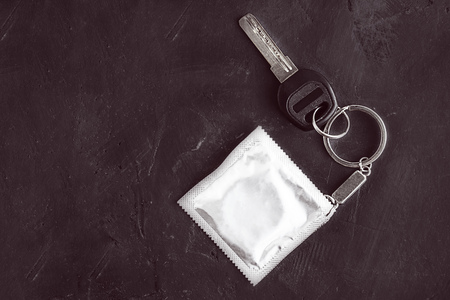 Key with keychain with grey foil moch up condom as fob on black empty chalkboard background with copy space, creative concept for safe sex, contraceptives always along with you and sexual educationの写真素材