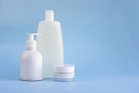 Three white plastic mockup bottles for shampoo or shower gel, dispenser and glass small tube for cream on lighnt blue empty background with copy space for text and designの写真素材