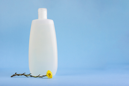 White plastic mockup bottle for shampoo or shower gel, dispenser, glass container for cream, flowers of healing herb foalfoot, Tussilago farfara on lighnt blue empty background with copy spaceの写真素材