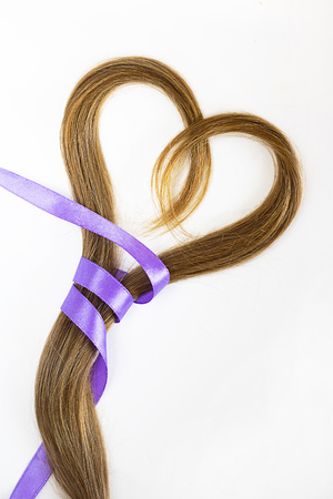 long blond hair donation put like heart with lavender ribbon as symbol of fight against cancer on white background. Top view. Natural material for making wig for patients. Vertical, isolated.の写真素材
