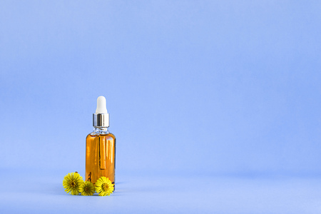 Glass mockup bottle with orange oil and flowers of healing herb foalfoot or Tussilago farfara on lighnt blue empty background with copy space for design about cosmetics, skin care, sun screen.の写真素材