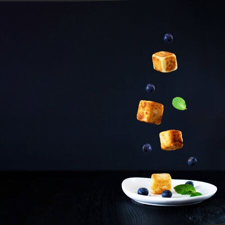 three cottage cheese cubes, blueberries and mint leaves falling down one is on white plate, on black background, sweet tasty dish for breakfast, Square with copy space for text or design, Levitationの写真素材
