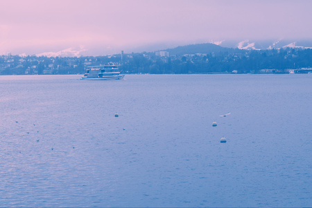 Stemboat on the Lake of Zurich with the background of foggy mountains with snowy tops. Wintertime. Scenery. Blue and grey colours. Sightseeing. Travelling.の写真素材