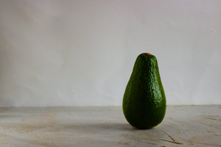 Green fresh avocado standing on white and grey plain empty background. Horizontal with copy space...