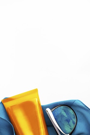 Orange mock up bottles of sun screen and sunglasses on bright contrast blue beach wrap on vertical blank white background with copy space. Holiday flat layの写真素材