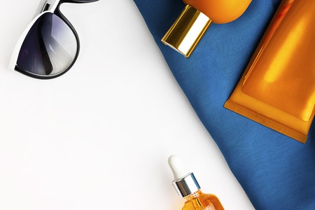 Orange mock up bottles of sun screen and sunglasses on bright contrast blue beach wrap on horizontal blank white background with copy space. Holiday flat layの写真素材