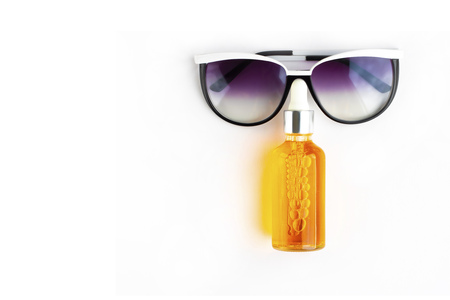 Orange bottle of sun screen oil with dark blue sunglasses put like human face on horizontal empty white background with copy space. Holiday contemporary flat lay. man skin care concept.の写真素材