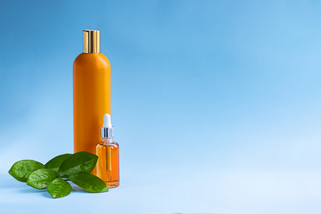 two mockup orange bottles and green leaves next to them on blue background. Sun screen effect cosmetics. Horizontal with copy space. Beauty, health care and skin, hair protection, UV filter.の写真素材