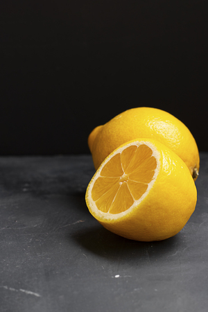 Half of lemon in focus and whole lemon behind on plain black backgroundの写真素材