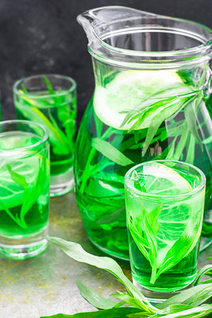 Summer cold green drink with tarragon, mint and lemon in glass decanter and small shots with ice,...