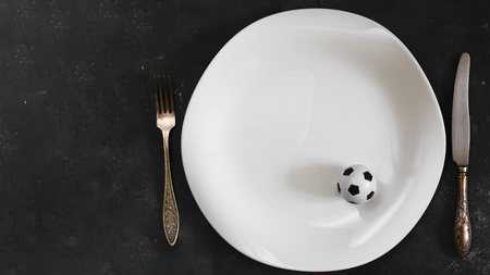 Small football ball on White plate with fork and knife on textured chalkboard background. Creative concept of diet and sport, special dietary plan for sportsmen. Horizontal with copy space. top viewの写真素材