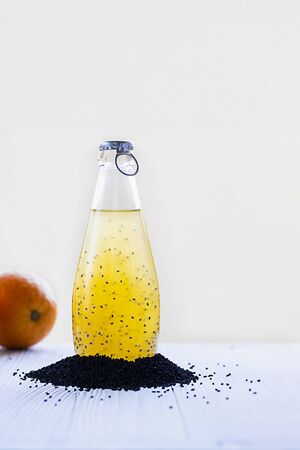 Colorful summer drink with basil seeds in bottle with blue cap surraounded with black basilica grains and defocused orange on background Vertical, copy space. Healthy beverage, superfood, detox, veganの写真素材