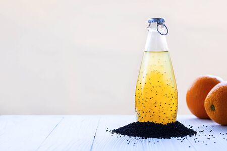Colorful summer drink with basil seeds in bottle with blue cap surraounded with black basilica grains and defocused orange on background Horizontal copy space Healthy beverage, superfood, detox, veganの写真素材