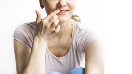 Red bubbles of virus herpes on lips of a woman in light pink t-shirt, lower part face is seen, which she touches with her finger. Medicine, treatment. Horizontal with copy space. White backgroundの写真素材