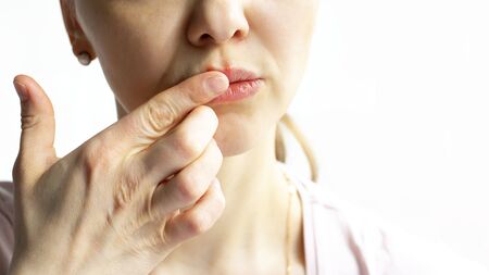 Red bubbles of virus herpes on lips of a woman in light pink t-shirt, lower part face is seen, which she touches with her finger. Medicine, treatment. Horizontal with copy space. White backgroundの写真素材