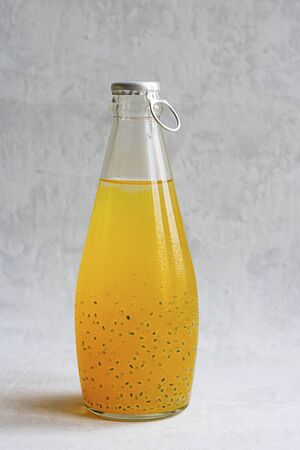 Orange citrus refreshing summer drink with basil seeds in bottle with metal cap on grey cement background. Vertical Healthy beverage, superfood, detox, veganの写真素材
