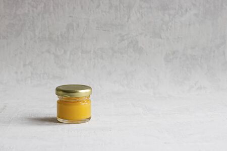 Small glass jar with metal cap with light yellow honey isolate on grey cement background with copy space. Healthy product, natural, Horizontalの写真素材