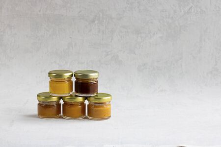 Five Small glass jar with metal cap with different kinds and colours of honey one on another isolate and on grey cement background with copy space. Healthy product, natural. Horizontalの写真素材