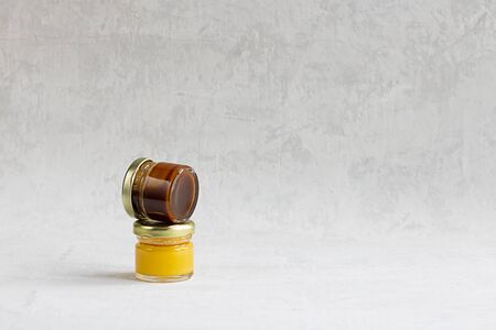 Two Small glass jar with metal cap with light yellow and dark brown honey one on another isolate on grey cement background with copy space. Healthy product, natural, Horizontalの写真素材