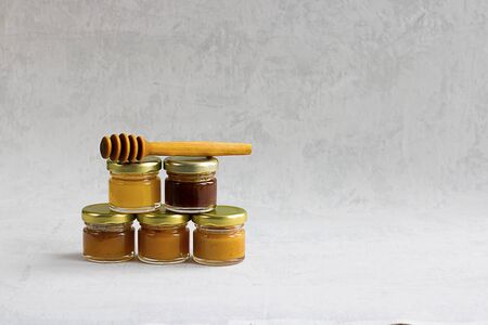 Five Small glass jar with metal cap with different kinds and colours of honey one on another and spoon isolate and on grey cement background with copy space. Healthy product, natural. Verticalの写真素材