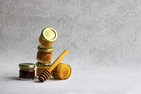 Five Small glass jar with metal cap with different kinds and colours of honey one on another and spoon isolate and on grey cement background with copy space. Healthy product, natural. Verticalの写真素材