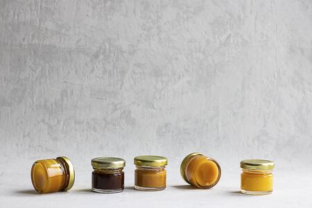 Five Small glass jar with metal cap with different kinds and colours of honey put in line isolate and on grey cement background with copy space. Healthy product, natural. Horizontalの写真素材